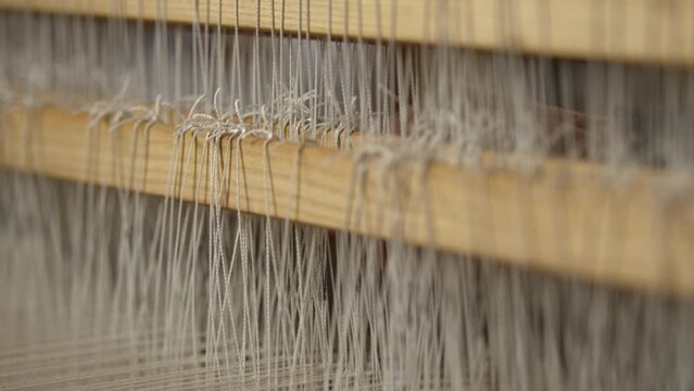 Person weaving with white threads on weaving machine rack-focus