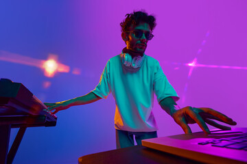 Young stylish man, DJ skillfully blending music on DJ mixer against gradient pink purple background in neon light. Concept of music, performance, festival, live concert