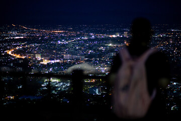 High-angle view of city lights at night, a blurred person standing and admiring the city...