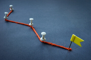 Concept of achieving goals, planning and stages. Orange thread, pins and flag.