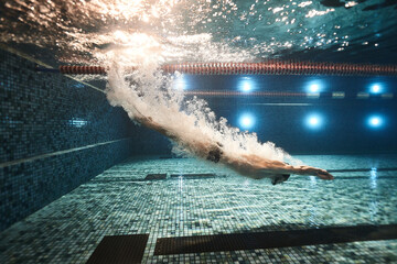 guy athlete swimmer jumps into the water in the pool and swims through air bubbles underwater...