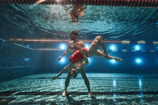 young athletes swimmers dive in the pool and under the water the guy holds the girl in his arms. synchronized swimming and posing. advertising underwater photography - Powered by Adobe