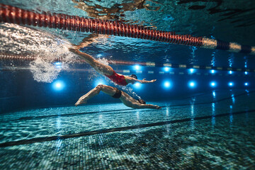 beautiful athletes swimmers guy and girl synchronously swim underwater in the pool on top of each...