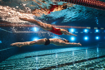 beautiful athletes swimmers guy and girl synchronously swim underwater in the pool on top of each...