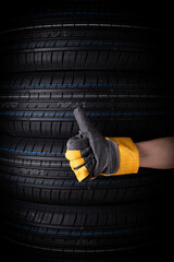 Hand in yellow gloves and car tires on black background, closeup.