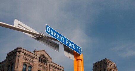 Dynamic city street corner showcasing Queen's Park sign, with clear blue skies. Street in view...