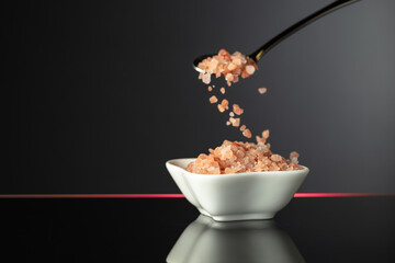 Pink Himalayan salt in a small ceramic bowl on a black reflective background.