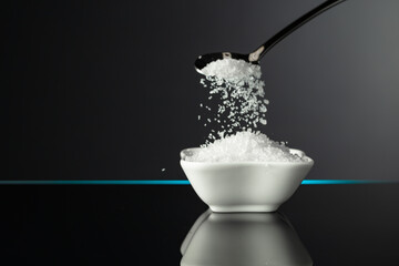 Sea salt in a small ceramic bowl on a black reflective background.