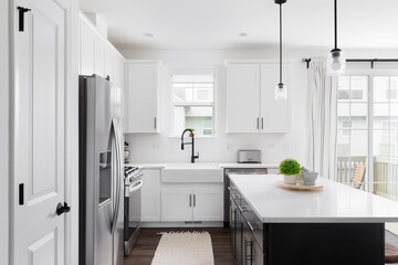 A modern farmhouse kitchen with white cabinets and a black island, stainless steel appliances,...
