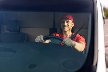 Happy european delivery man driving car and smiling, delivering parcels, front view - Powered by Adobe