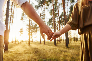 Close up view of hands. Happy couple is outdoors in the forest at daytime - obrazy, fototapety, plakaty