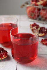Tasty pomegranate juice in glasses and fresh fruits on white tiled table, closeup