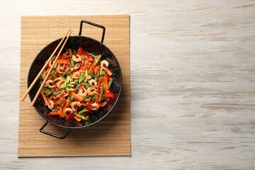 Shrimp stir fry with vegetables in wok and chopsticks on wooden table, top view. Space for text