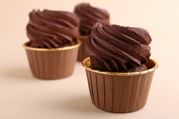 Delicious chocolate cupcakes on beige background, closeup
