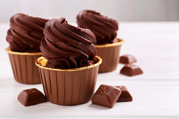 Delicious cupcakes and chocolate pieces on white wooden table, closeup