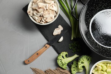 Wok pan, noodles and different vegetables on light grey table, flat lay. Space for text