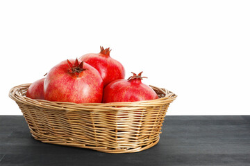 Fresh pomegranates in wicker basket on black wooden table against white background, space for text