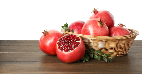 Fresh pomegranates in wicker basket and green leaves on wooden table against white background