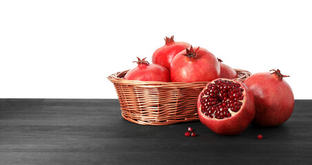 Fresh pomegranates in wicker basket on black wooden table against white background, space for text