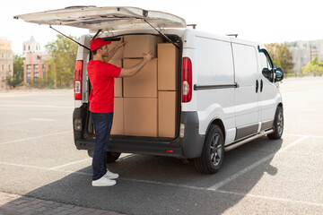 Courier man loading cardboard boxes to van, preparing for delivering postal parcel, outdoors shot