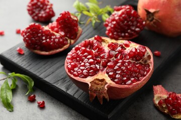 Cut fresh pomegranate and green leaves on grey table, closeup