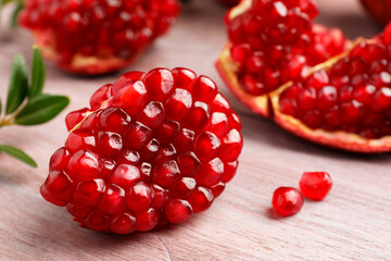 Cut fresh pomegranate and green leaves on wooden table, closeup