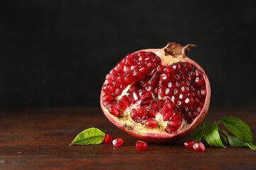 Cut fresh pomegranate and green leaves on wooden table, space for text
