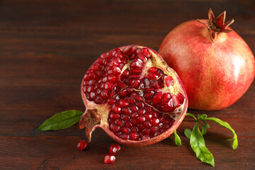 Fresh pomegranates and green leaves on wooden table, closeup