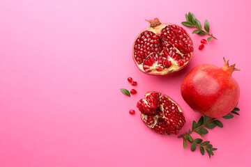 Fresh pomegranates and green leaves on pink background, flat lay. Space for text