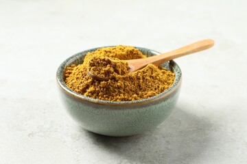 Dry curry powder in bowl and spoon on light table, closeup