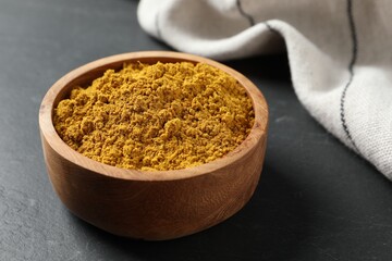 Dry curry powder in bowl on dark textured table, closeup
