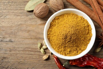 Dry curry powder in bowl and other spices on wooden table, flat lay. Space for text