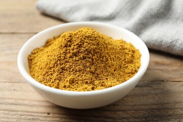 Dry curry powder in bowl on wooden table, closeup