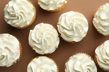 Tasty vanilla cupcakes with cream on dark beige background, top view