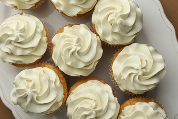 Tasty vanilla cupcakes with cream on table, flat lay