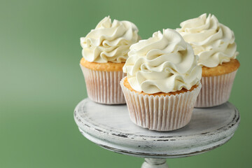 Tasty vanilla cupcakes with cream on green background, closeup