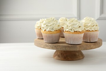 Tasty vanilla cupcakes with cream on white wooden table, space for text