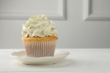 Tasty vanilla cupcake with cream on white table, closeup. Space for text