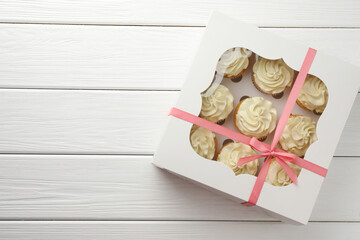 Tasty cupcakes with vanilla cream in box on white wooden table, top view. Space for text