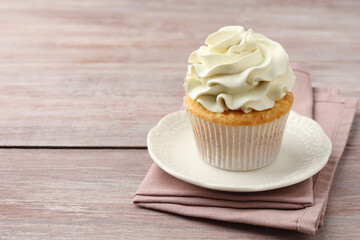 Tasty cupcake with vanilla cream on pink wooden table, closeup. Space for text