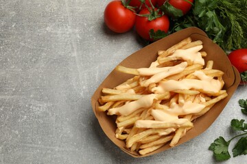 Tasty potato fries, cheese sauce in paper container and products on grey table, top view. Space for text