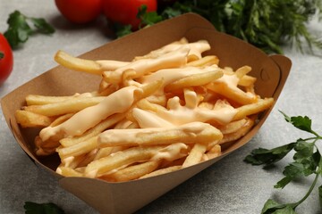 Tasty potato fries, cheese sauce in paper container and products on grey table, closeup