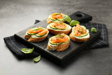 Tasty canapes with salmon, cucumber and cream cheese on grey table