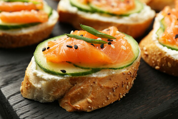 Tasty canapes with salmon, cucumber and cream cheese on table, closeup