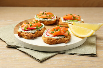 Tasty canapes with salmon, cucumber, radish and cream cheese on wooden table