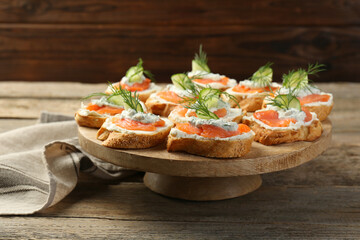 Tasty canapes with salmon, cucumber, cream cheese and dill on wooden table