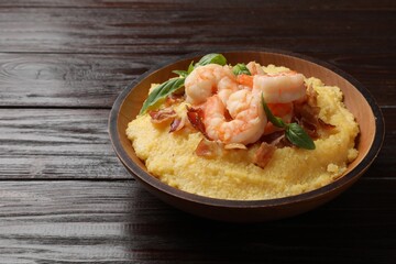 Fresh tasty shrimps, bacon, grits and basil in bowl on wooden table, closeup