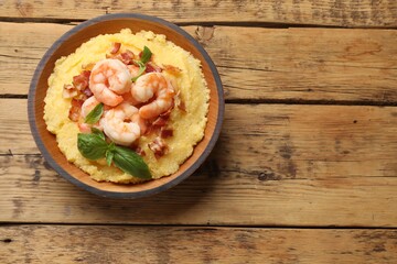 Fresh tasty shrimps, bacon, grits and basil in bowl on wooden table, top view. Space for text