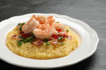 Plate with fresh tasty shrimps, bacon, grits, green onion and pepper on black table, closeup