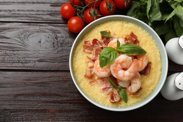 Fresh tasty shrimps, bacon, grits and basil in bowl on wooden table, flat lay. Space for text